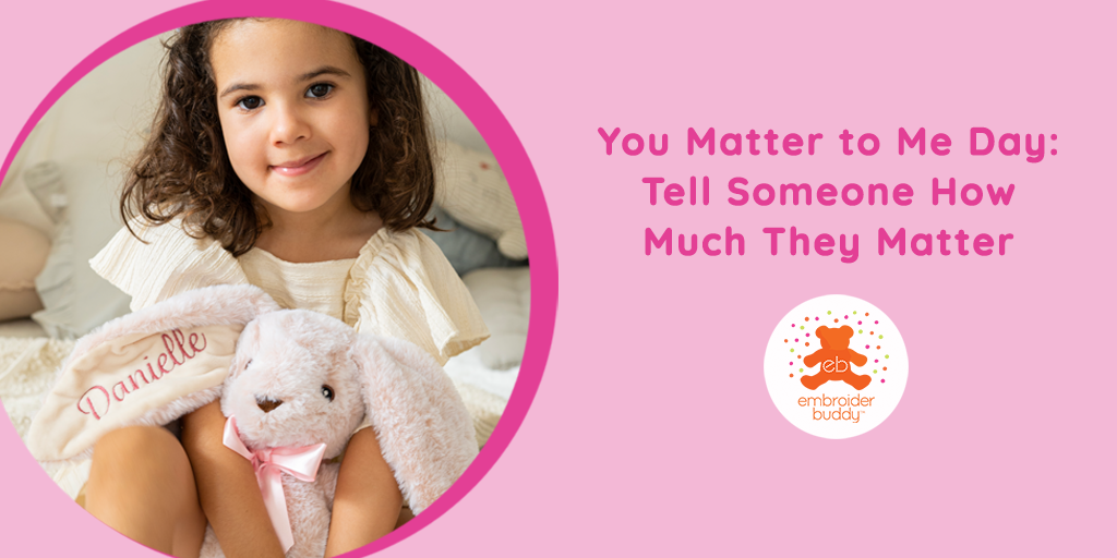 A sweet little brown haired girl holding a pink Big Ear Bunny with the ear embroidered with her name on a hero image for blog post called "You Matter to Me Day: Tell Someone How Much They Matter" which also shows the Embroider Buddy logo